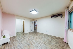 Una habitación amplia con suelo de madera con motivo de espiga, una lámpara de techo, un equipo de aire acondicionado y un banco blanco.