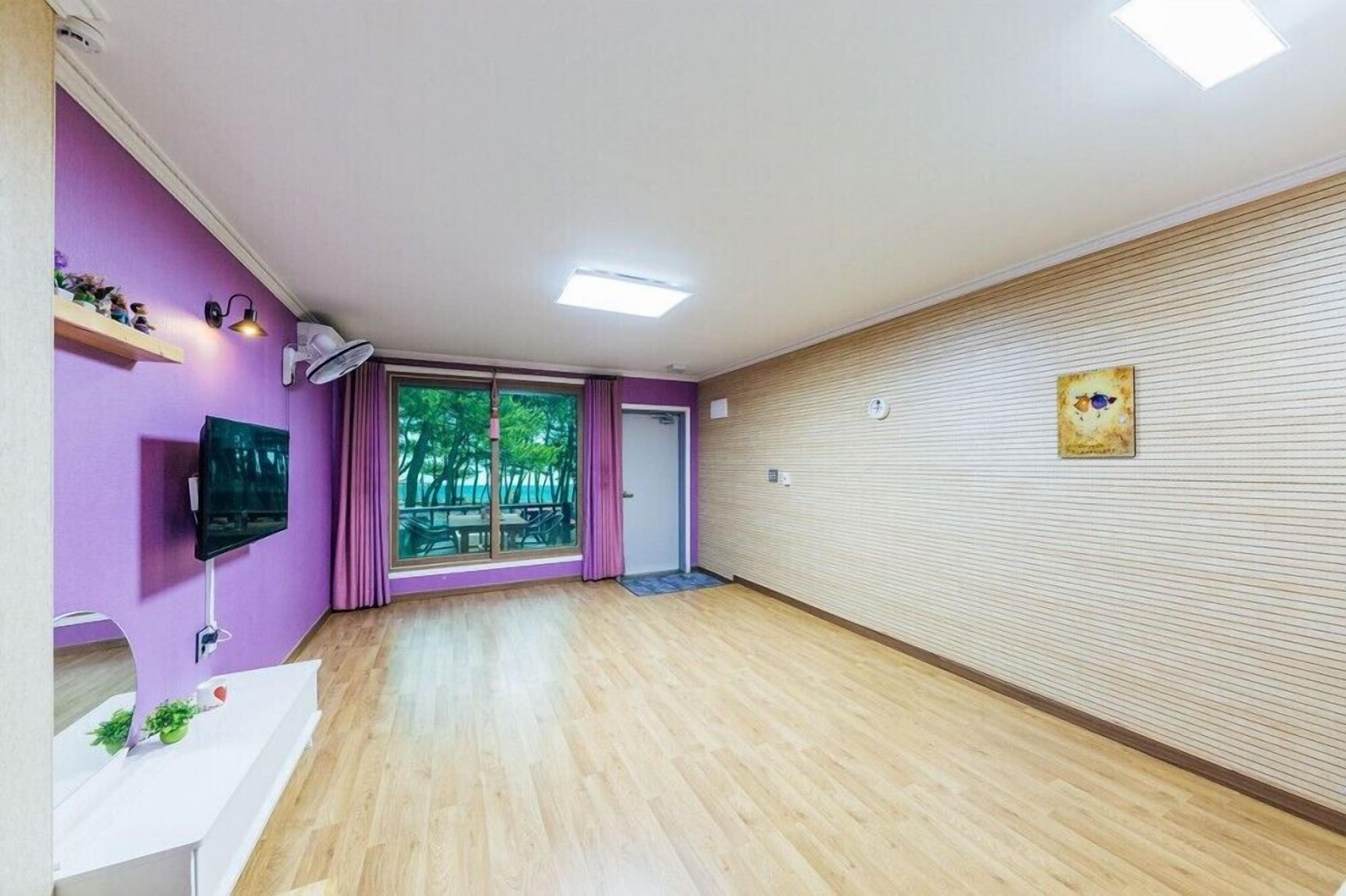 A spacious room with a large window, a flat-screen TV, and a wooden floor.
