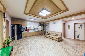 A spacious living area with a wooden floor, a beige sofa, a kitchen with modern appliances, and a ceiling with a skylight.