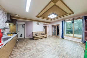 A spacious living area with a sofa, a kitchen with a red coffee machine, and large windows with curtains.