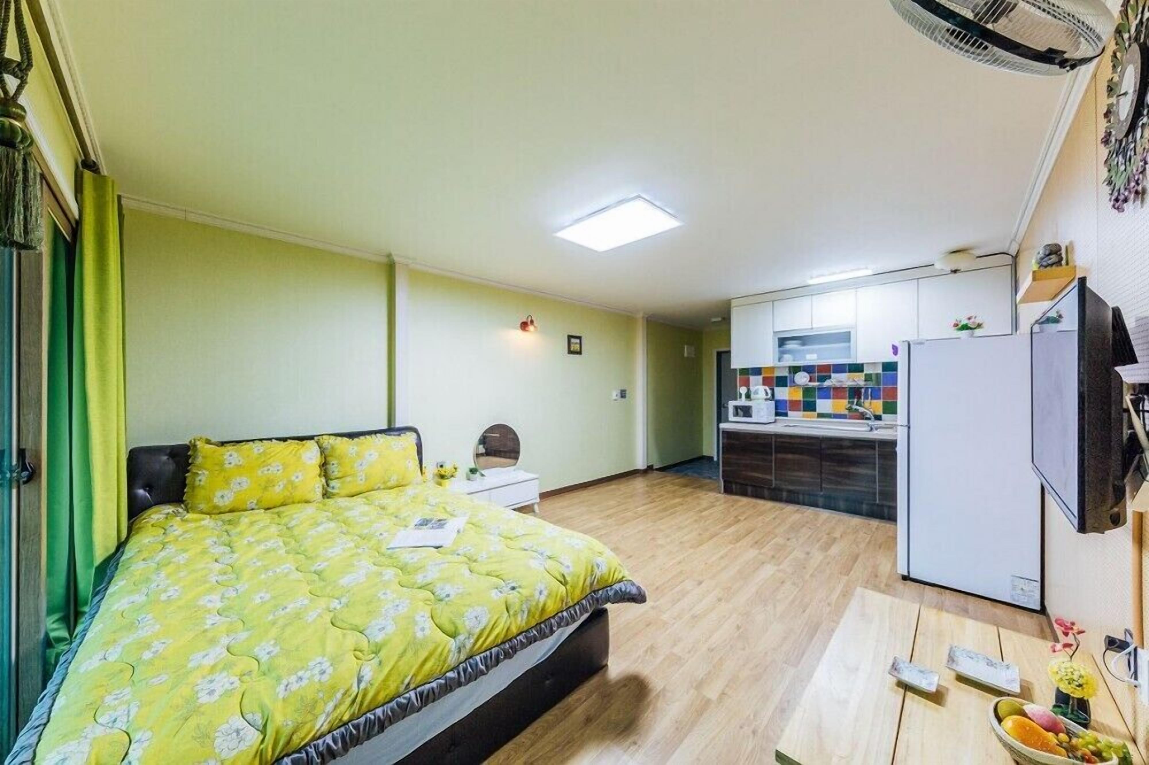 Une pièce de taille modeste comprenant un lit, une petite table, un coin cuisine et un ventilateur de plafond.