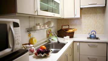 A kitchen with white cabinets, a microwave, a sink, and a kettle.