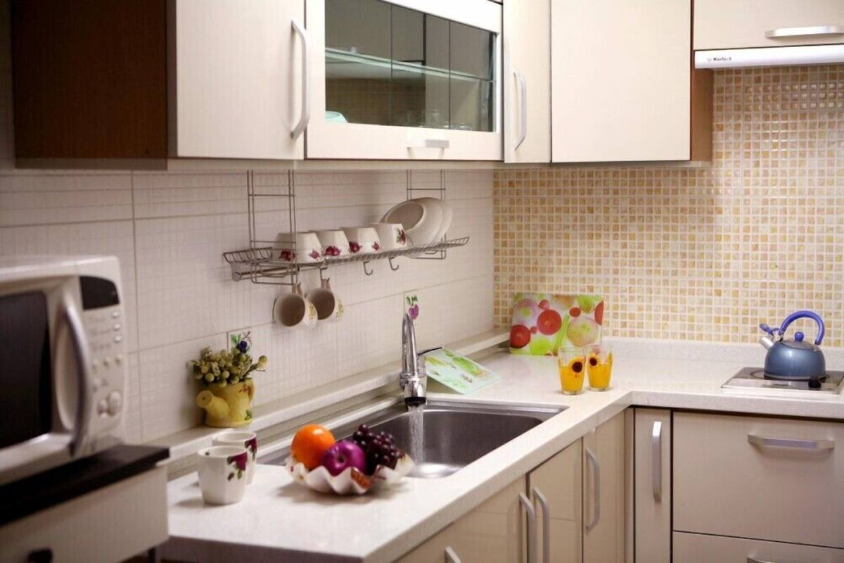 A kitchen with white cabinets, a microwave, a sink, and a kettle.