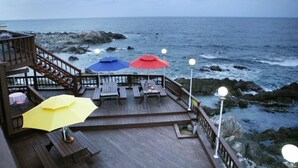 Un muelle de madera con mesas de picnic y sombrillas que da a una costa rocosa.