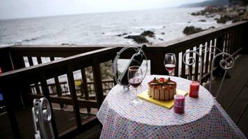 A table with a dessert, wine glasses, and candles on a deck overlooking the ocean.