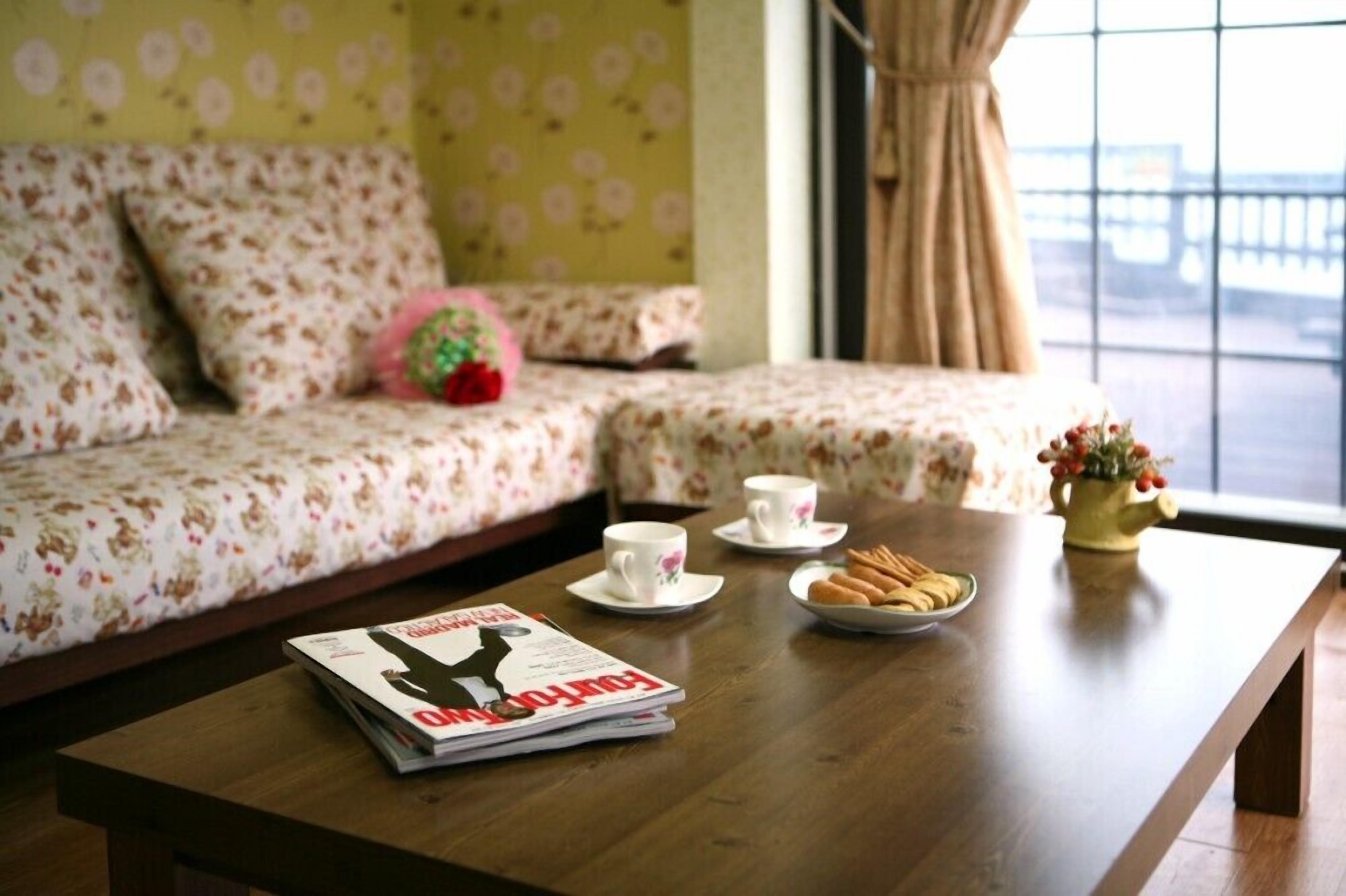 A cozy living area with a sofa, a coffee table with a magazine, cups, and snacks.