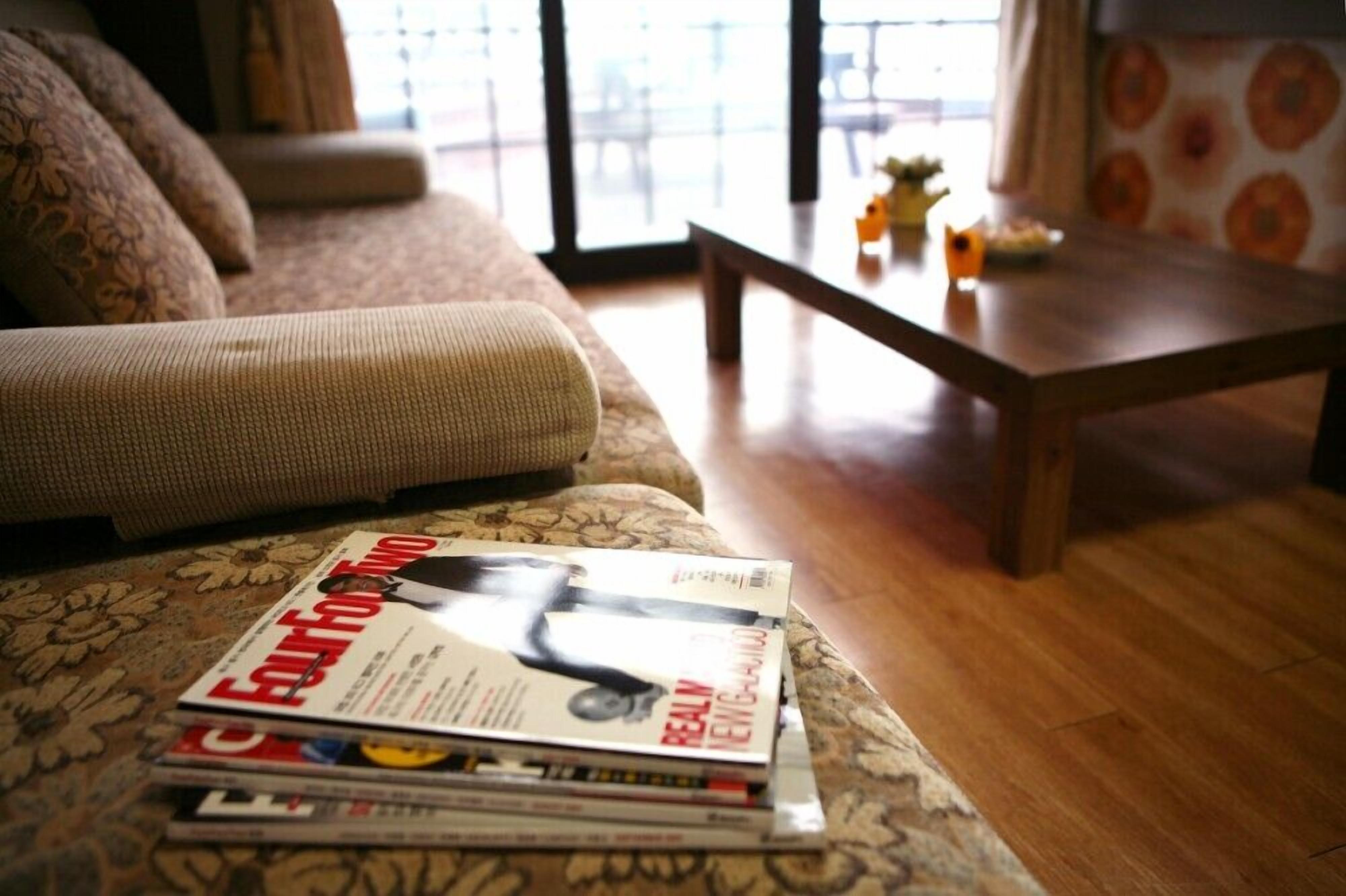 A living room with a sofa, a coffee table, and a stack of magazines.