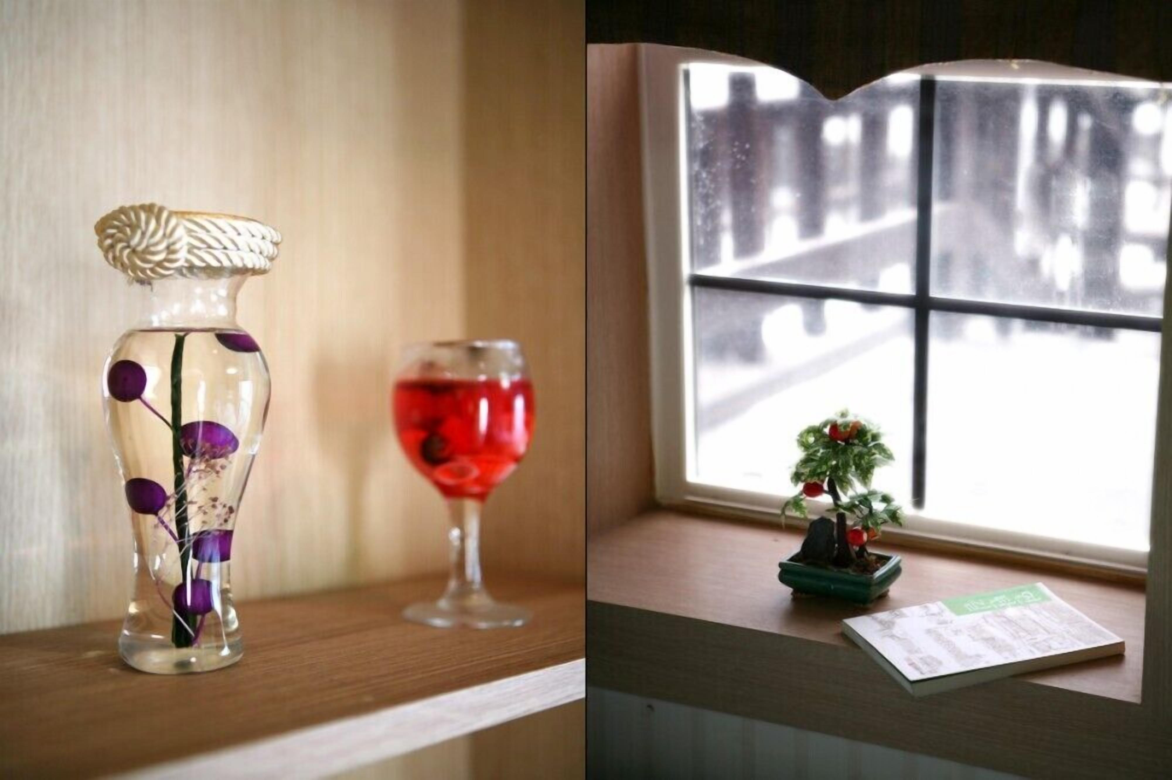 Een vaas met paarse details en een glas met rode vloeistof op een houten ondergrond.