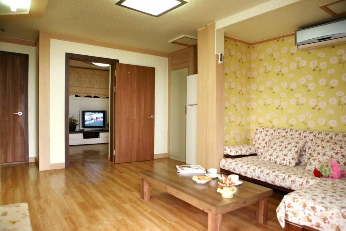 A living room with a wooden floor, a sofa with a floral pattern, a coffee table with items on it, and a television in the background.