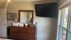 Una camera da letto con una cassettiera in legno, uno specchio, una TV a schermo piatto e una finestra vista all'esterno.