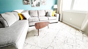 A living room with a grey sofa, a wooden coffee table, and a teal accent wall. - Johnny Cash "The Rambler" Suite on Main - walking distance to all stores and food! (Custer)