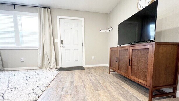 A room with a wooden floor, a white door, a television on a wooden cabinet, and a window with curtains. - Johnny Cash "The Rambler" Suite on Main - walking distance to all stores and food! (Custer)