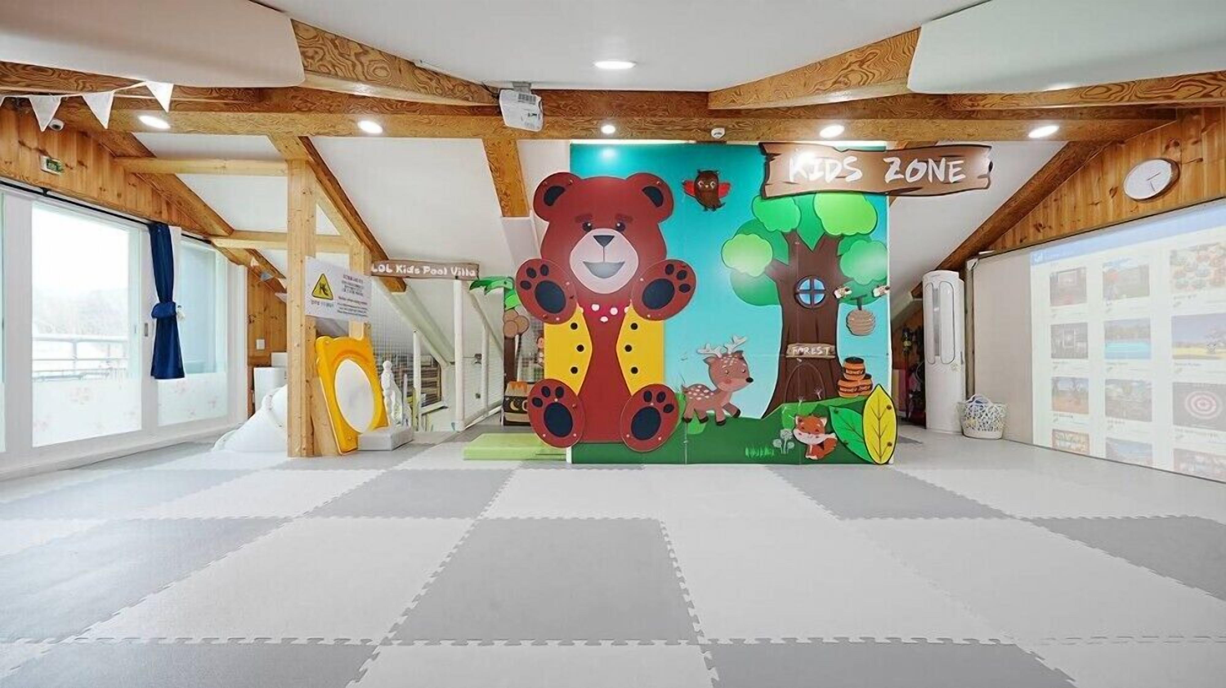 A children's play area with a large bear mural, a pool villa sign, and a 'Kids Zone' banner.