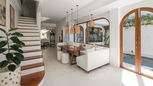 A modern living room with a staircase, a dining area, and a pool view. - The Arki Villa (Canggu)