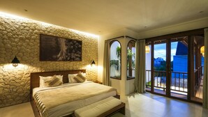 A bedroom with a stone wall, a large bed, a painting, and a view of the outside through a glass door. - The Arki Villa (Canggu)