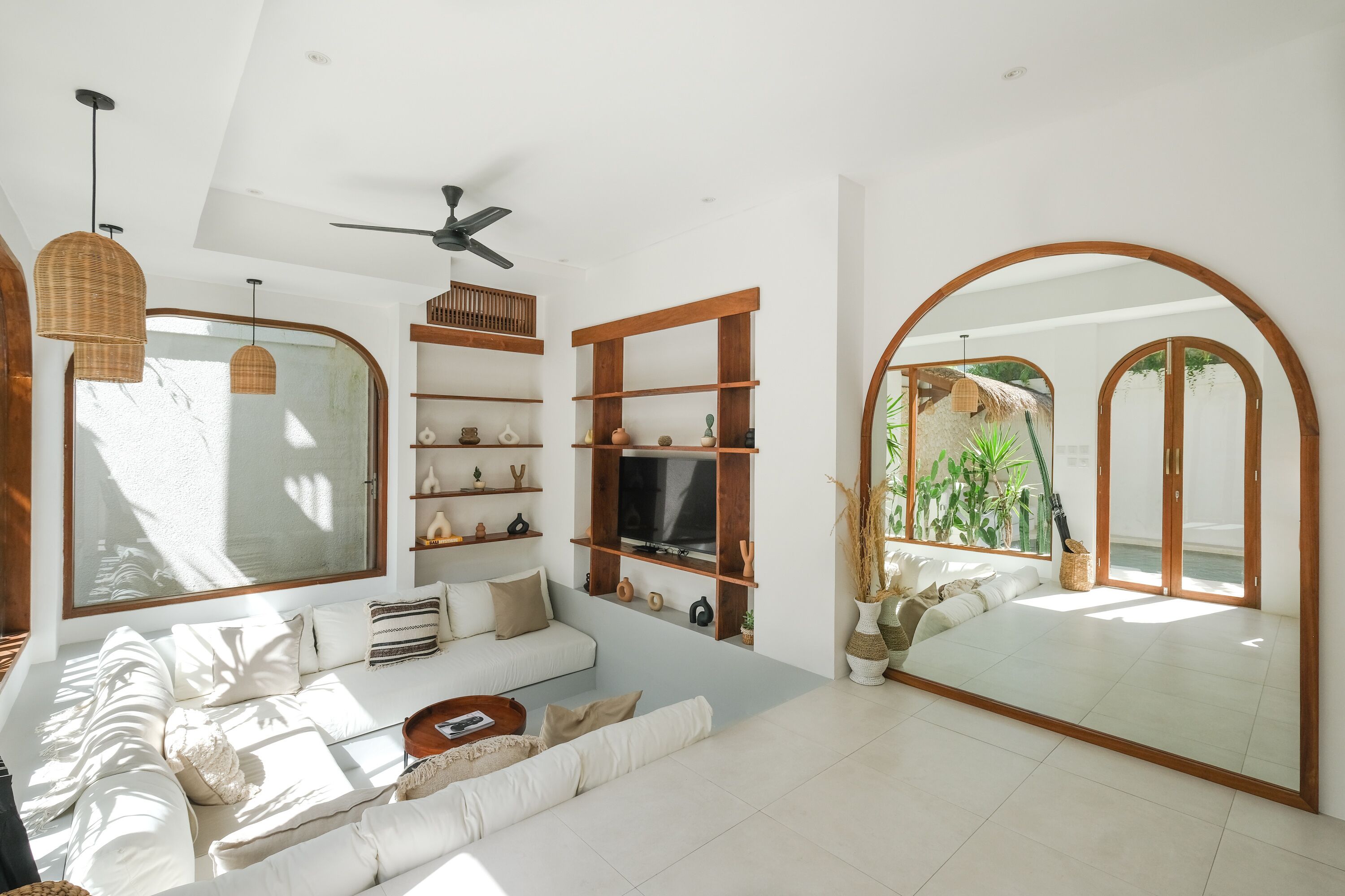 Un soggiorno moderno con una grande finestra, una ventola a soffitto ed elementi decorativi su scaffali a muro.