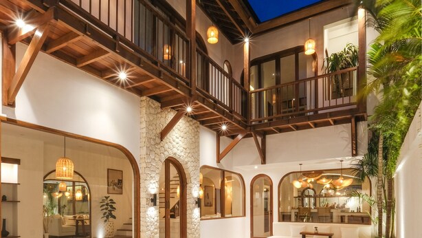 A modern pool area with a stone wall, wooden deck, and a balcony overlooking the pool. - The Arki Villa (Canggu)