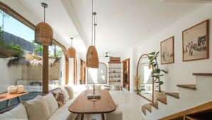A modern living room with a wooden dining table, white sofas, and a large window overlooking a pool. - The Arki Villa (Canggu)
