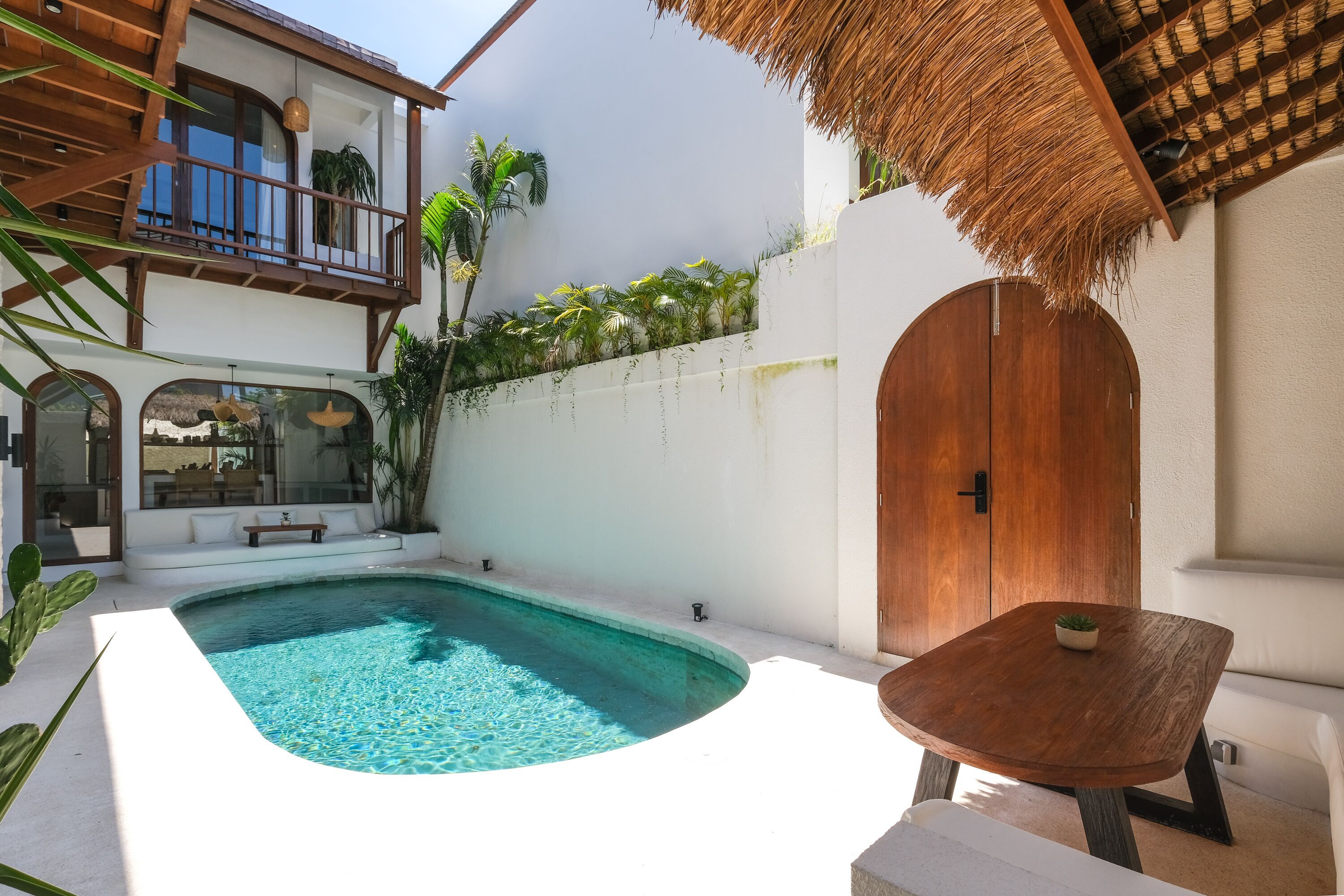 A pool area with a wooden table and a thatched roof structure.