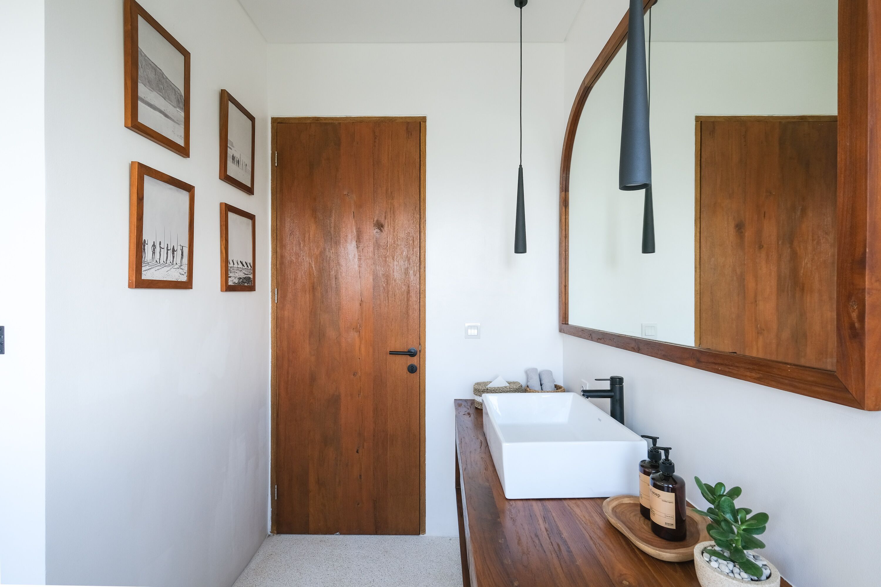 A bathroom with a wooden door, a white sink, a mirror, and framed pictures on the wall.