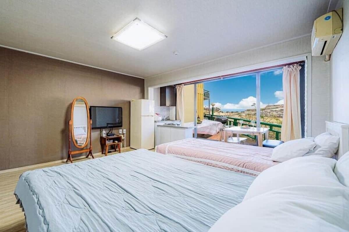 A hotel room with a large bed, a TV, a mirror, a small kitchenette, and a balcony with a view.