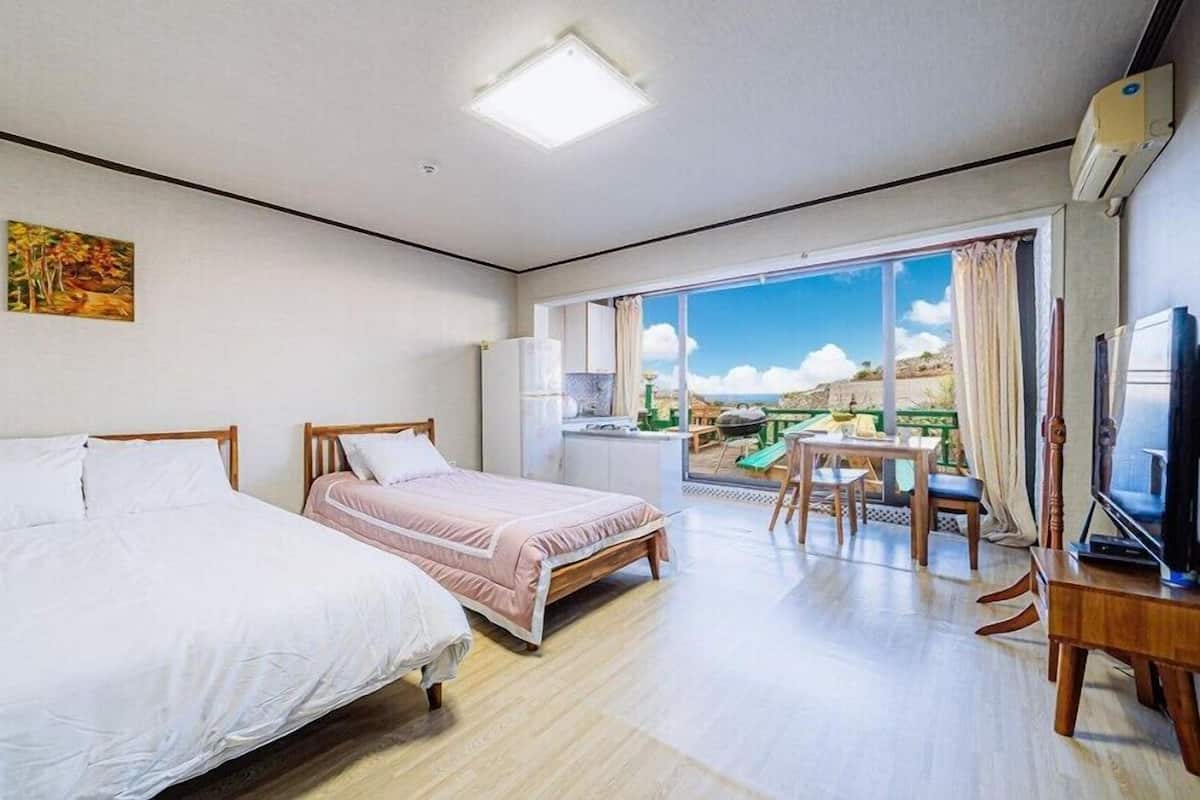 A hotel room with two beds, a kitchenette, a balcony with a table and chairs, and a TV.