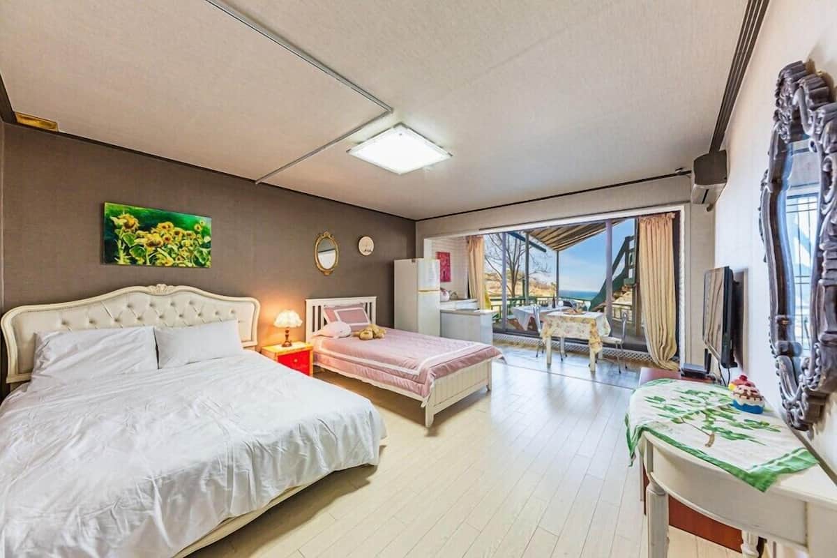 A bedroom with a large bed, a smaller bed, a desk, and a view of the outdoors.
