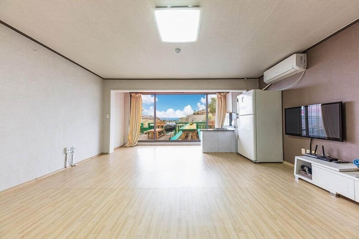 A spacious living area with a large window, a flat-screen TV, and a built-in air conditioning unit.