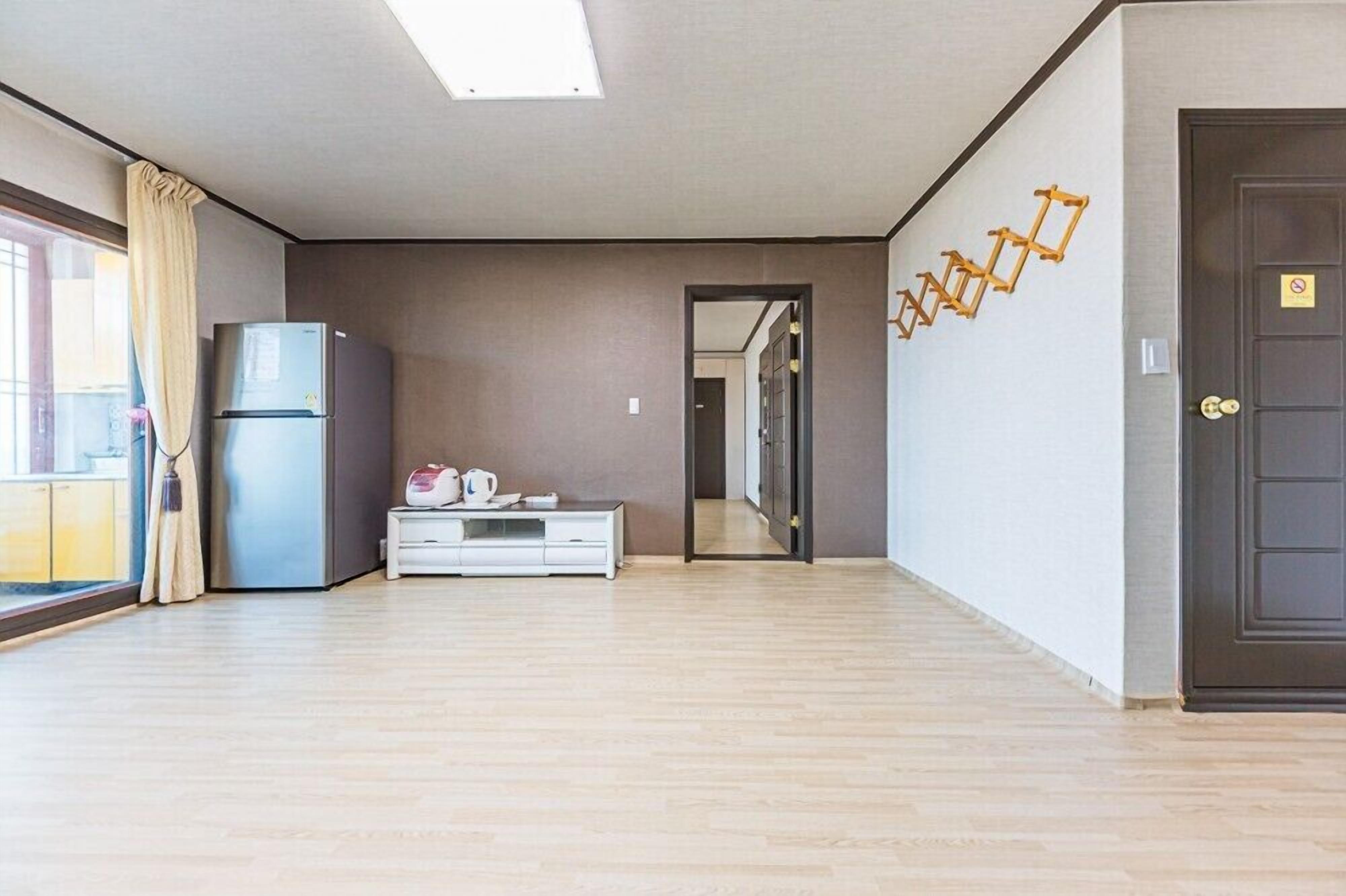 A modern living room with a large window, a refrigerator, a white cabinet, and a door with a no-smoking sign.