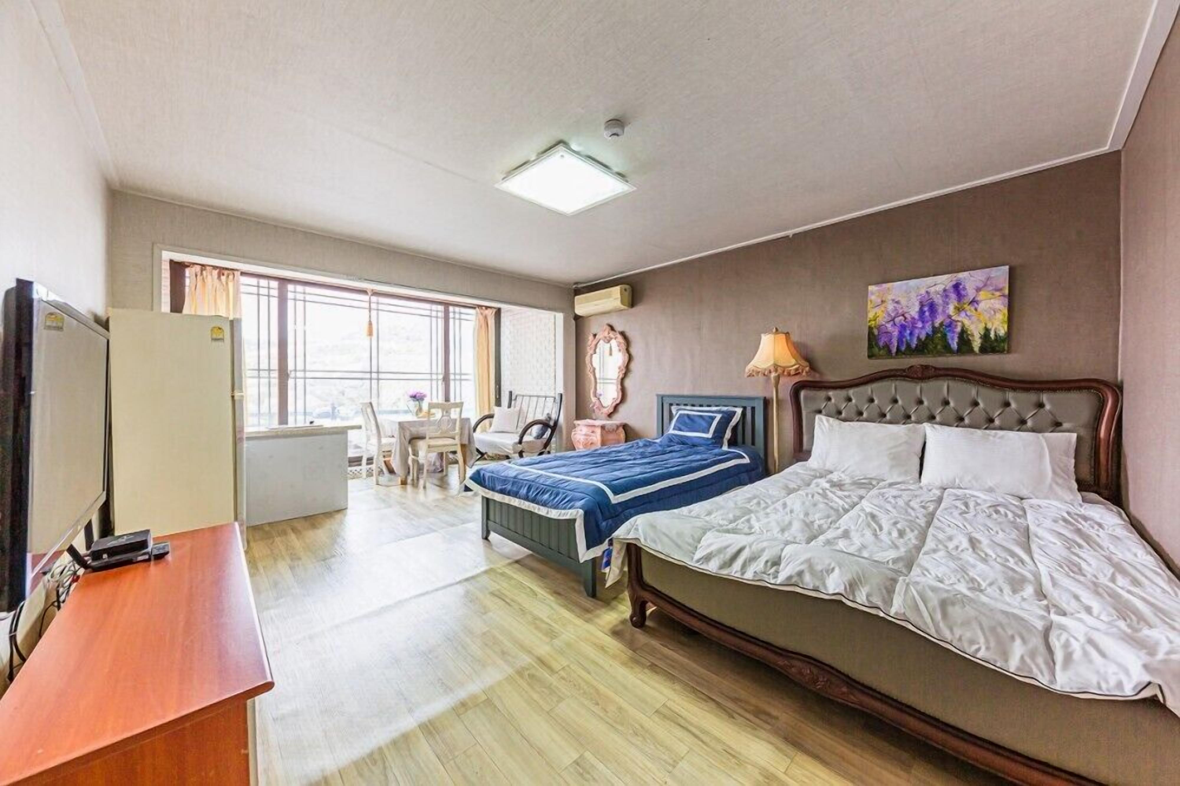 A hotel room with a bed, a desk, a chair, a TV, and a window.