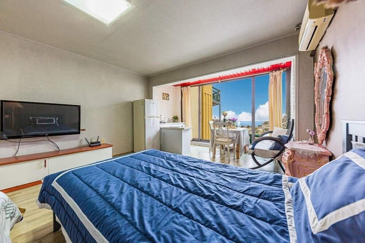 A hotel room with a bed, a television, a desk, a chair, and a view of the outdoors.