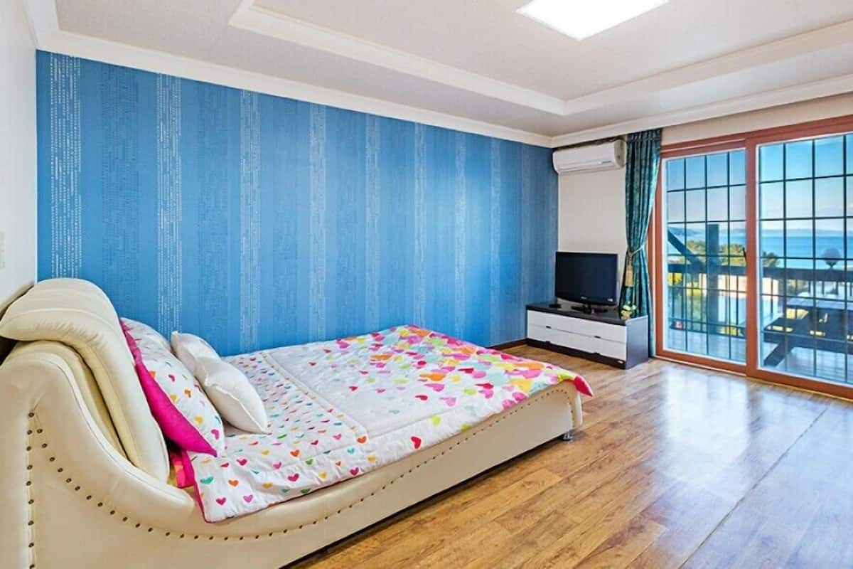 A bedroom with a bed, a TV, and a view of the sea through a sliding glass door.