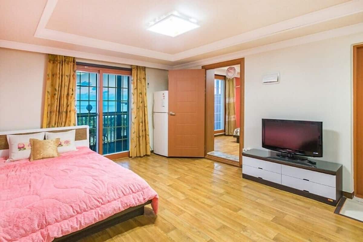 A bedroom with a bed, a television, and a sliding door leading to a balcony.