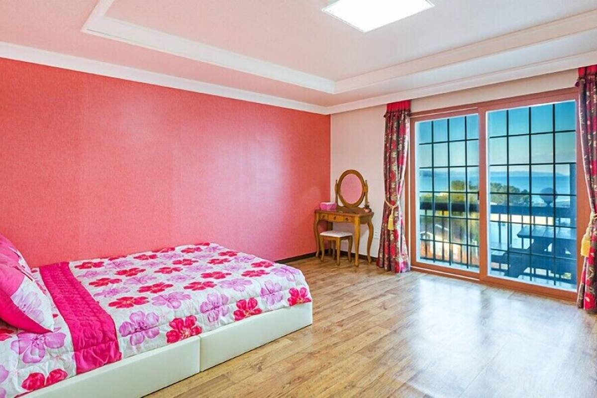 A bedroom with a bed, a vanity with a mirror, and a large window with a view.