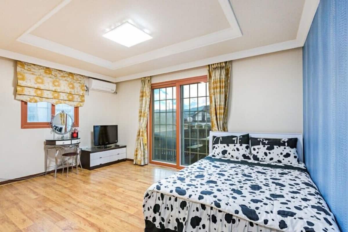 A bedroom with a bed, a television, a desk, and a window with curtains.