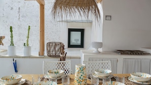 A dining area with a wooden table set for a meal, surrounded by white chairs and a thatched ceiling. - 3162 Casa Meraki by Barbarhouse (Gallipoli)