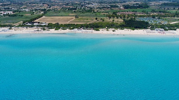 An aerial view of a coastal area with a beach, a sports field, and a residential area with houses and greenery. - 3162 Casa Meraki by Barbarhouse (Gallipoli)