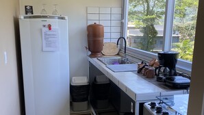 Eine kleine Küche mit Kühlschrank, Spüle, Herd und einem großen Fenster mit Blick auf Grünflächen.