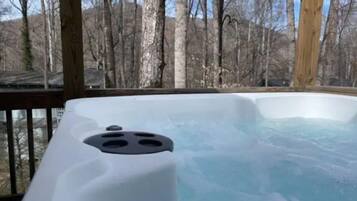 Un jacuzzi en una terraza de madera con vistas a árboles desprovistos de hojas.