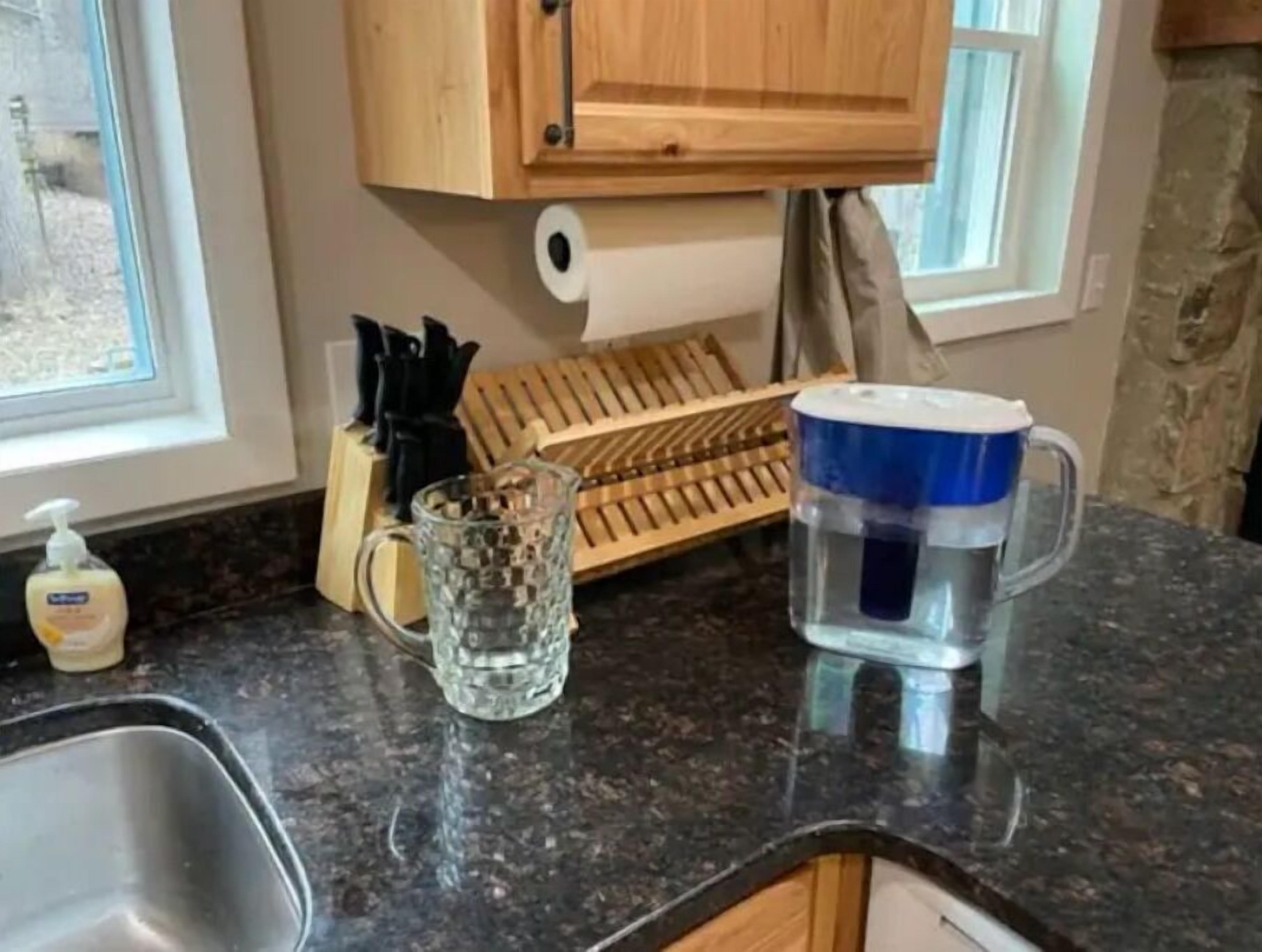 Una encimera de cocina con un lavamanos, un utensilero de madera, un vaso y un dispensador de agua.