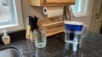Una encimera de cocina con un lavamanos, un utensilero de madera, un vaso y un dispensador de agua.