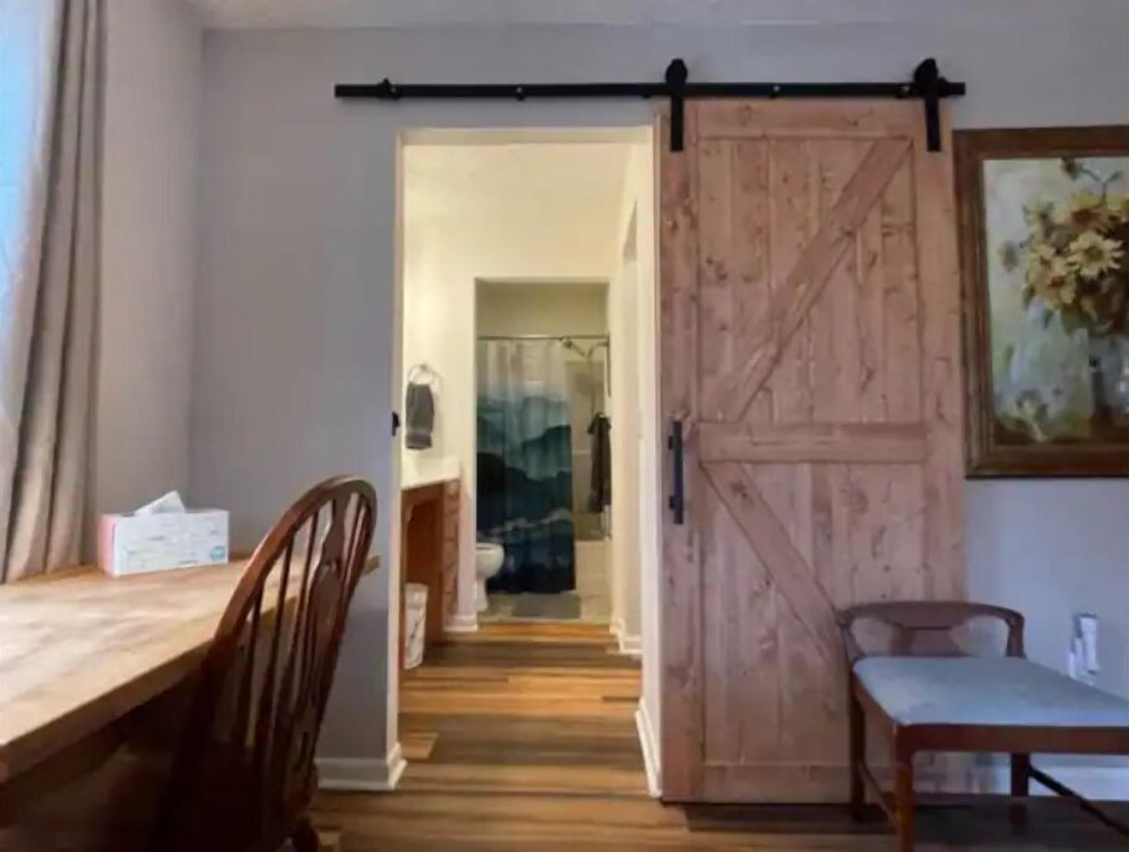 A room with a wooden floor, a dining table with chairs, a sliding barn-style door, and a painting on the wall.