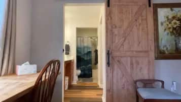 A room with a wooden floor, a dining table with chairs, a sliding barn-style door, and a painting on the wall.