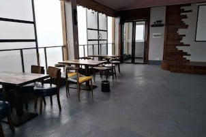 A dining area with tables and chairs, large windows, and a staircase.