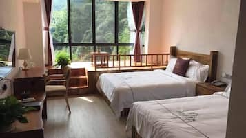 Habitación de hotel con dos camas, un escritorio con lámpara, una silla y vistas al bosque a través de amplios ventanales.