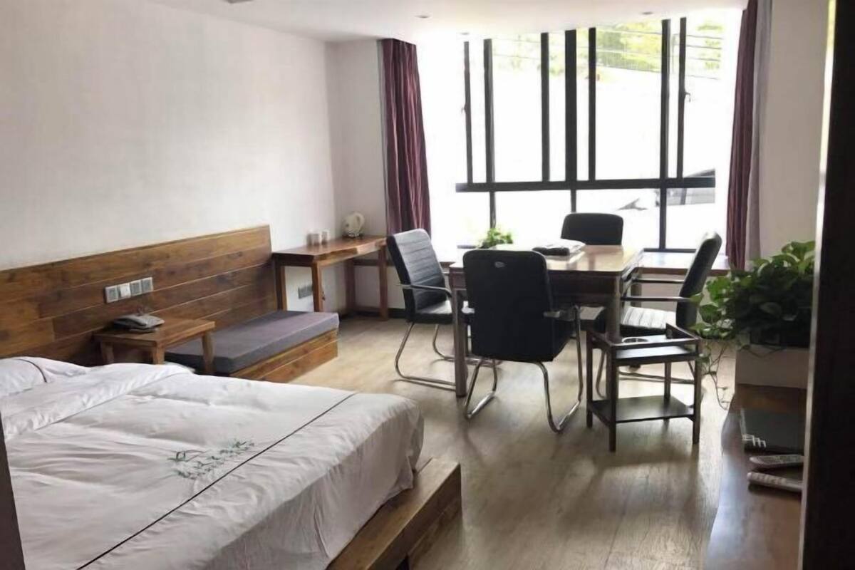 Hotellihuone, jossa on sänky, työpöytä, kaksi tuolia, penkki ja ikkuna, jossa on verhot.