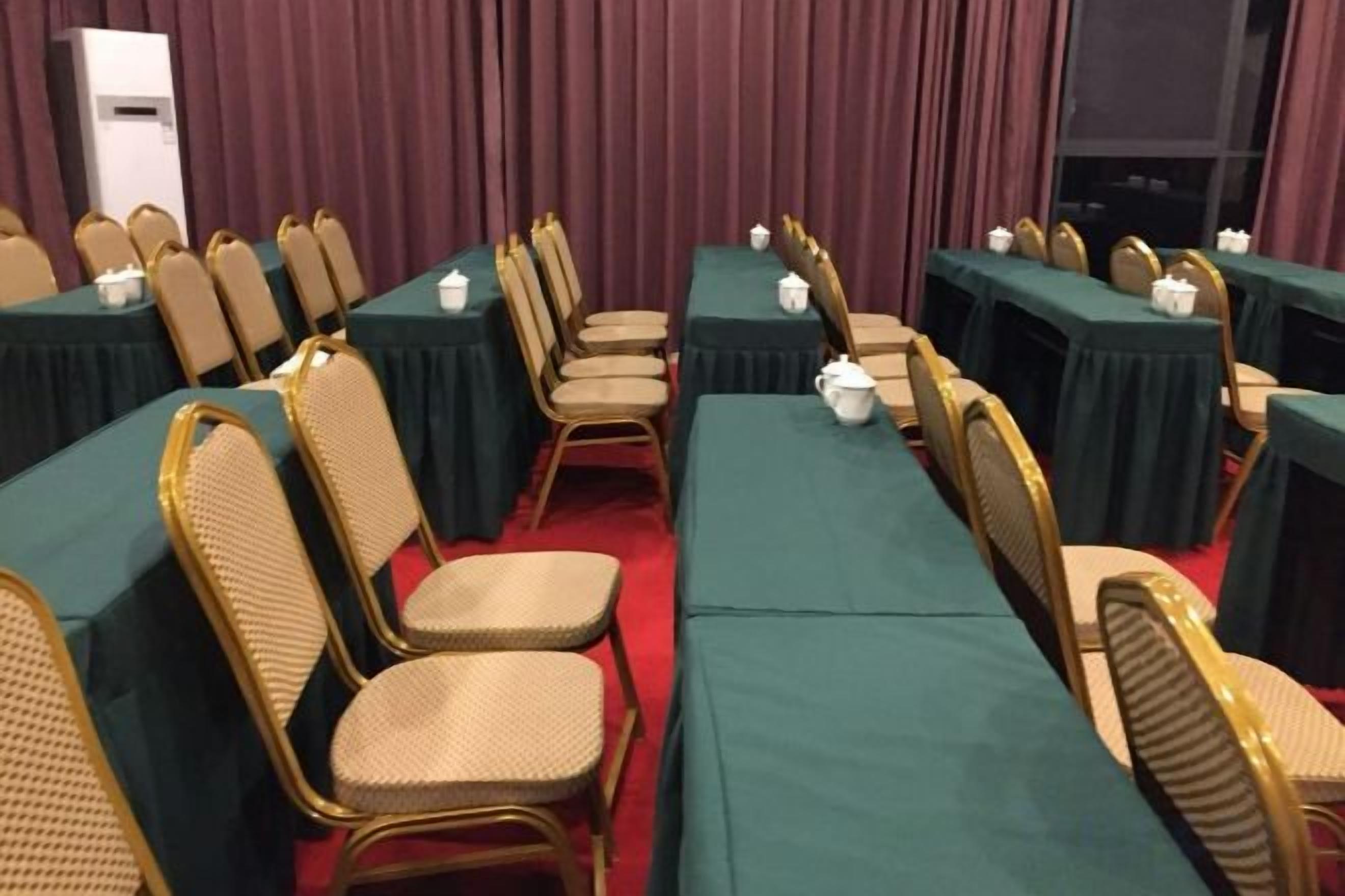 Une salle de conférence avec des rangées de tables et de chaises, un tapis rouge et un grand écran à l’avant.