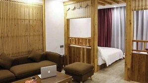 A room with a wooden partition, a bed with a white bedspread, a brown sofa, a small table with a laptop, and a red curtain. - Senlinli Campsite (Zixing)