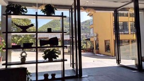 A modern interior with a glass door leading to an outdoor area, shelves with potted plants, and a view of a building with a yellow facade. - Senlinli Campsite (Zixing)