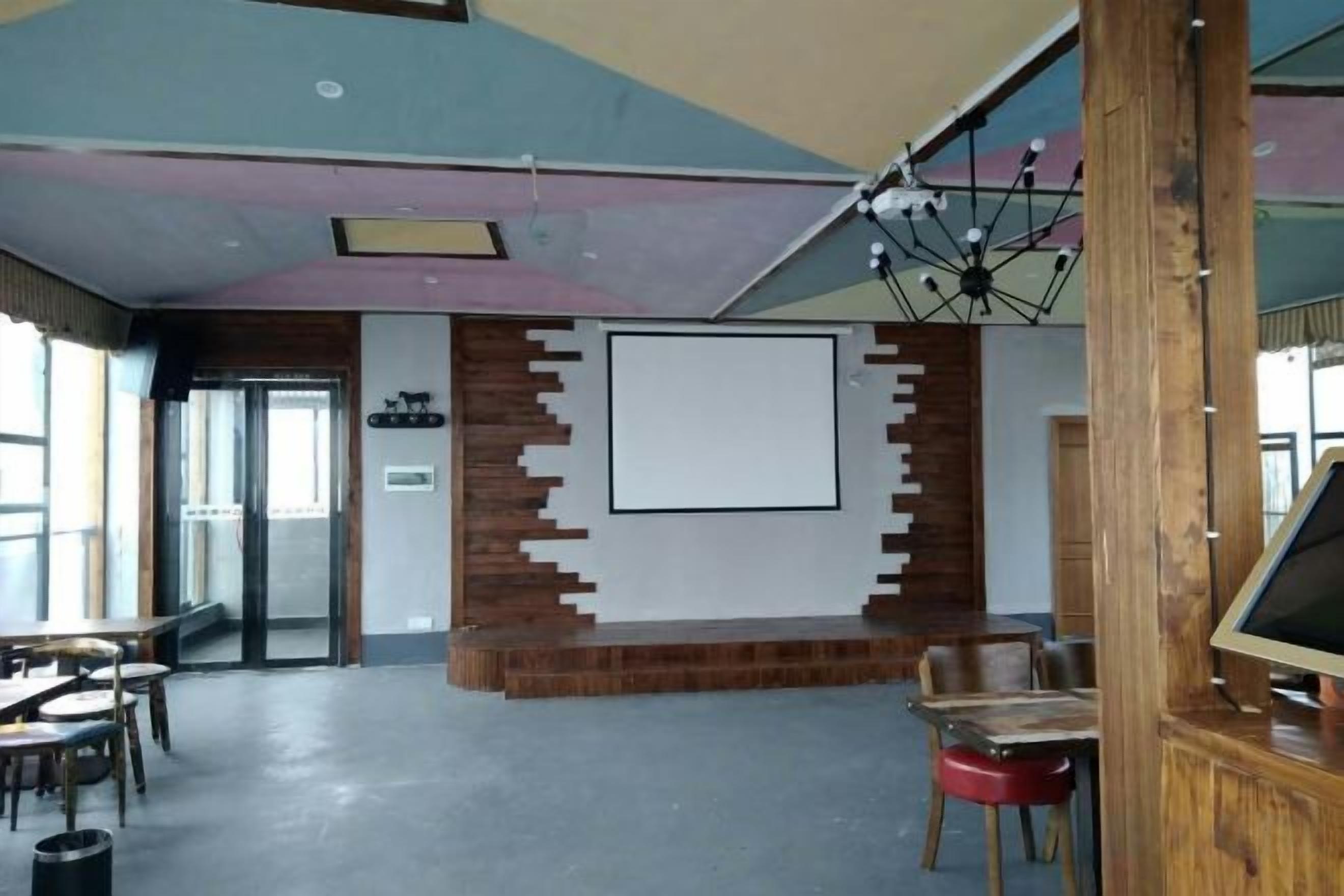 Une salle de conférence dotée d’un grand écran, de quelques éléments décoratifs en bois et d’un luminaire au plafond.